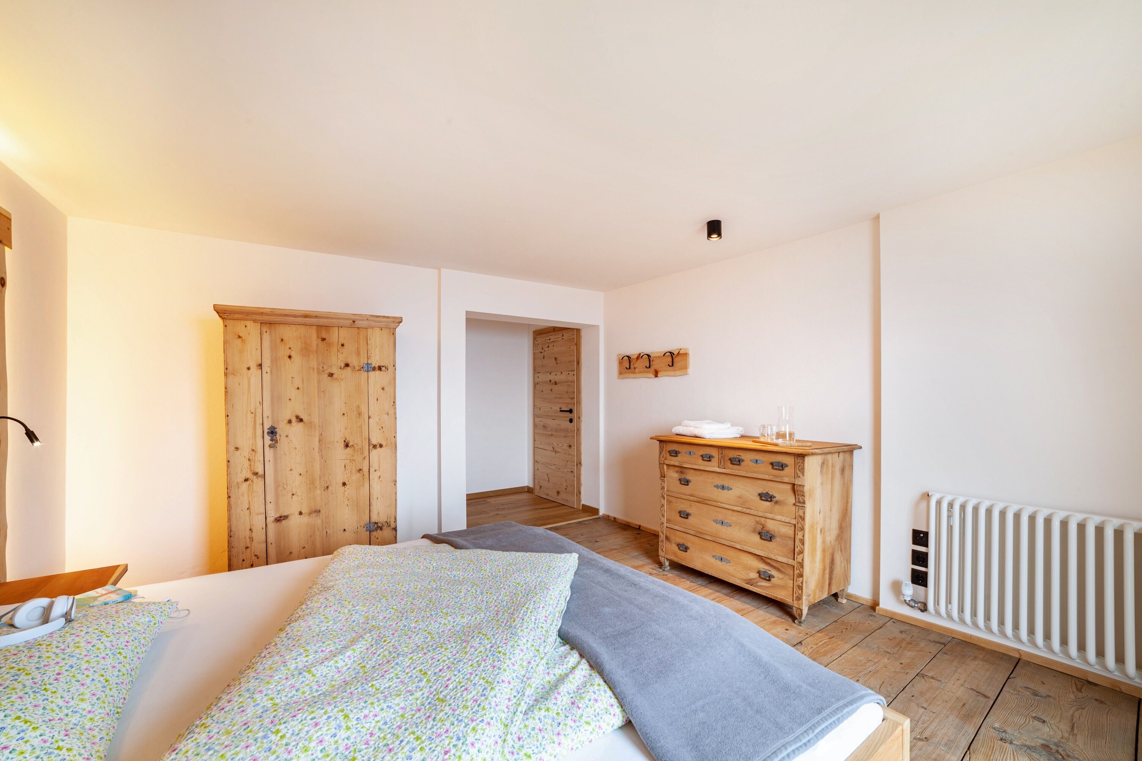 A bedroom with a bed, wooden wardrobe, dresser, and a radiator.