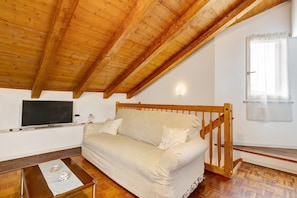 A room with a wooden ceiling, a sofa, a television, and a window with curtains.