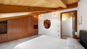 A bedroom with a wooden ceiling, a bed with white bedding, a wooden wardrobe, and a mirror on the wall.