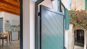 An open door leading to a room with a kitchen, a dining area, and a staircase with a wrought iron gate.