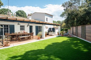 Una casa blanca con techo de tejas, un patio con mesa y sillas, y un césped bien cuidado.