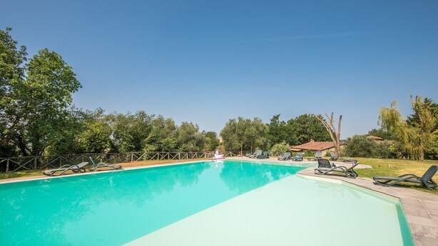 Ein rechteckiger Swimmingpool mit glasklar blauem Wasser, umgeben von einer Holzterrasse und Liegestühlen.