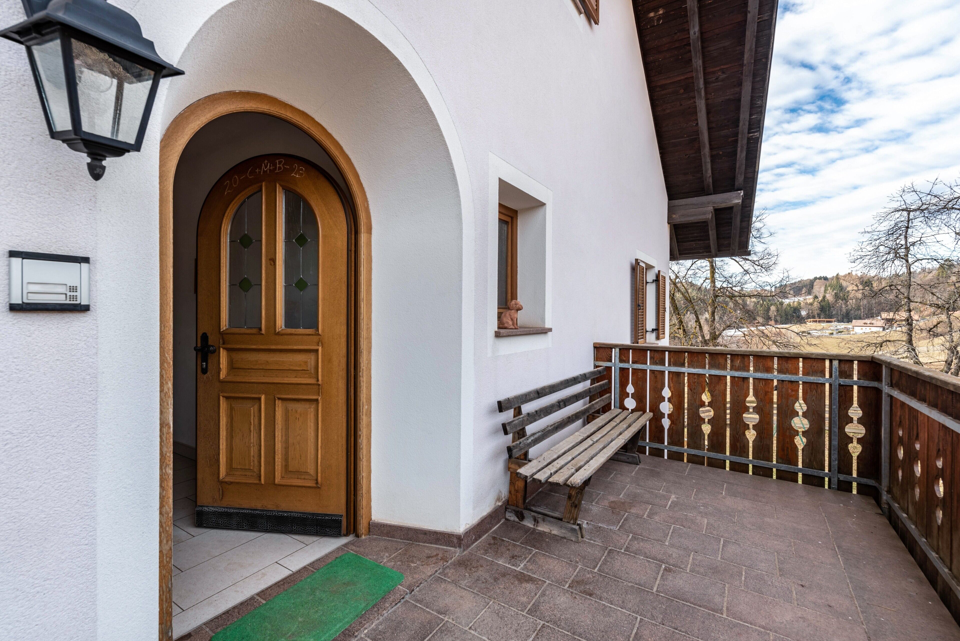 A white building with a wooden door, a bench, and a balcony with a railing.