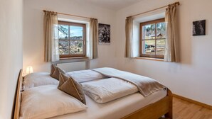 Een slaapkamer met twee bedden, grote ramen met gordijnen, een radiator en uitzicht op de omgeving.