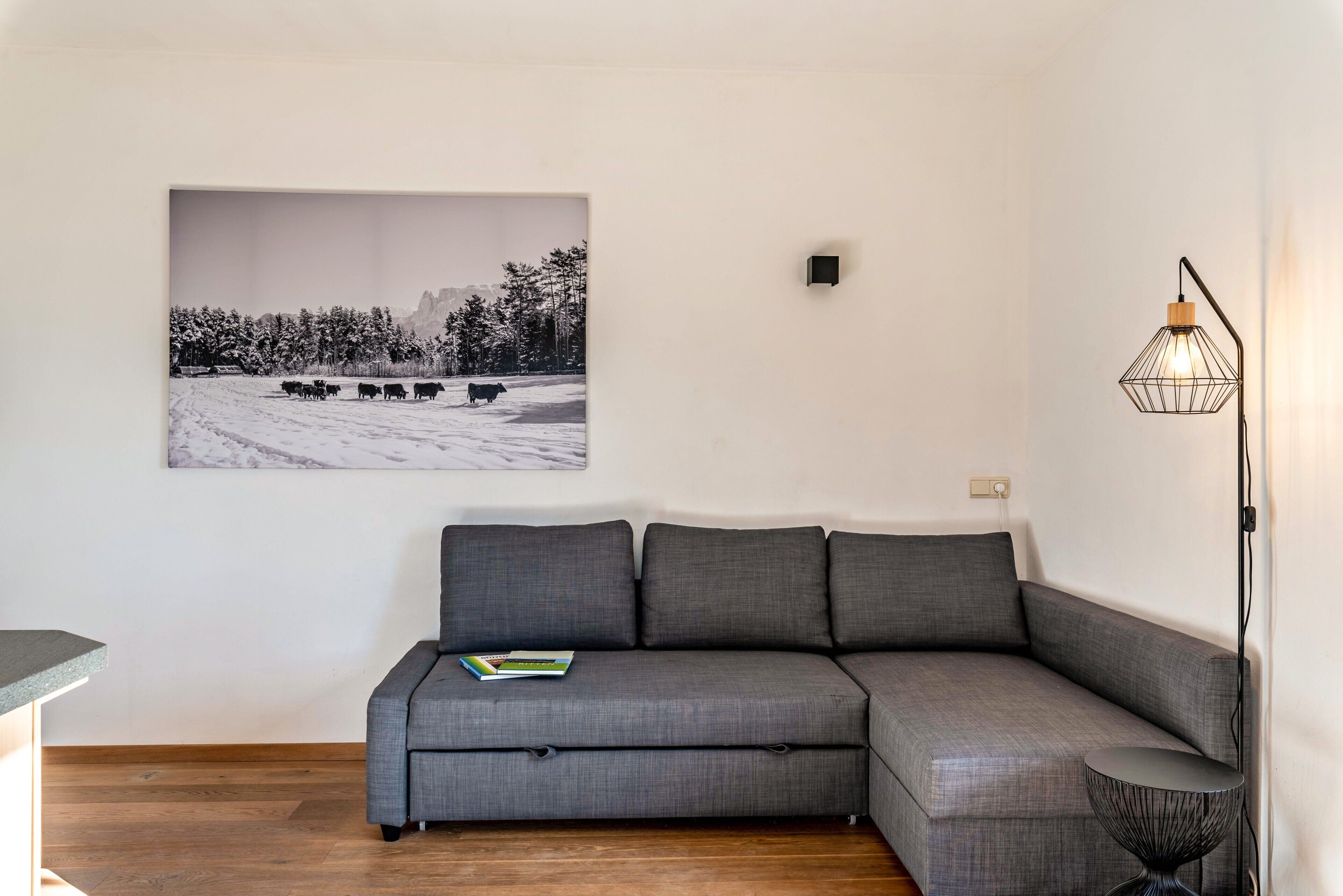 Un salon moderne avec un canapé d’angle gris, une photographie en noir et blanc encadrée, une lampe sur pied et une petite table ronde.