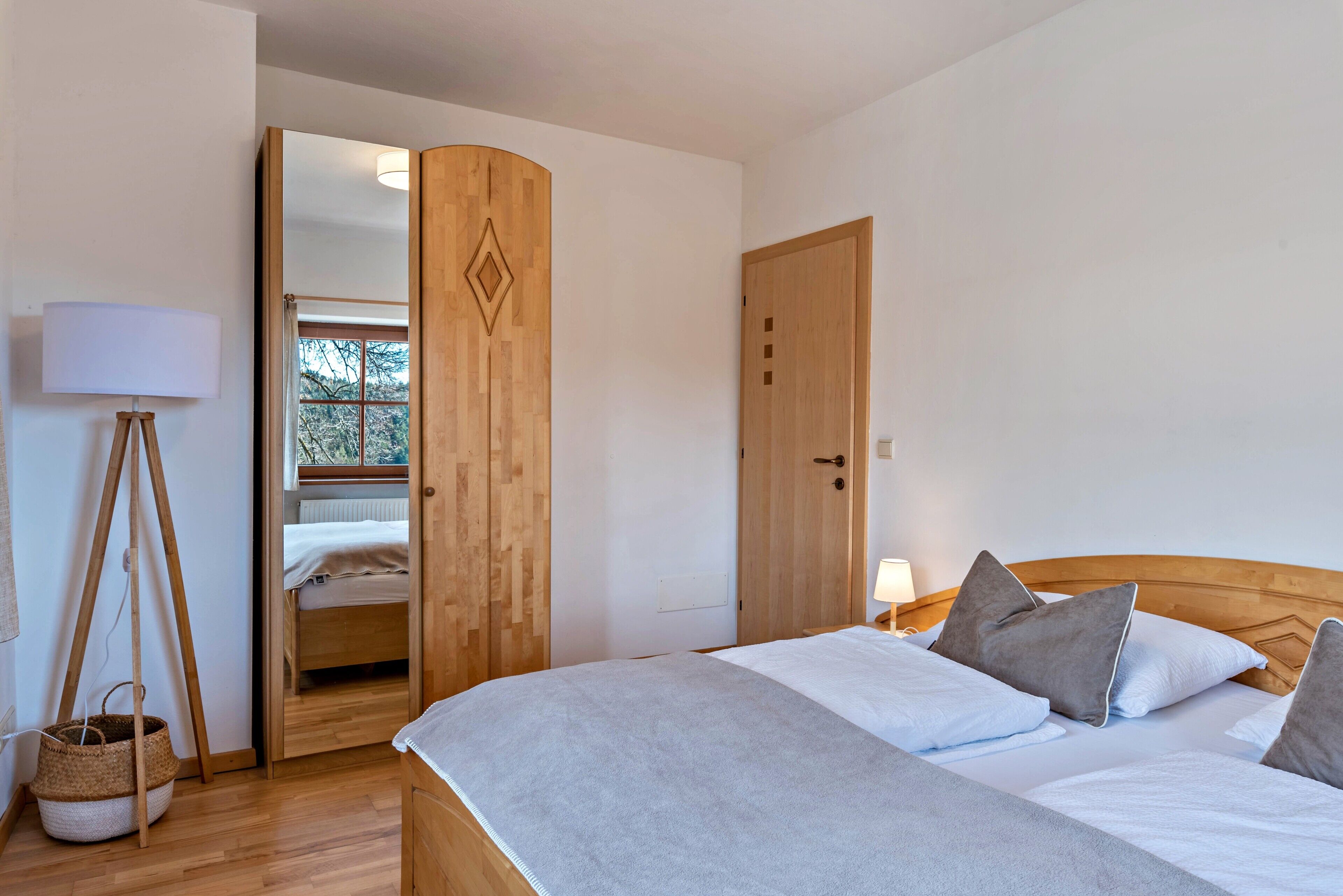 A bedroom with a wooden bed, a bedside table with a lamp, a wooden wardrobe, and a mirror.