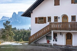 A building with a wooden balcony, a red door, and a mountain view in the background.