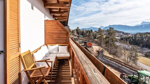 Een balkon met houten meubels, uitzicht op bergen en een trein in de verte.