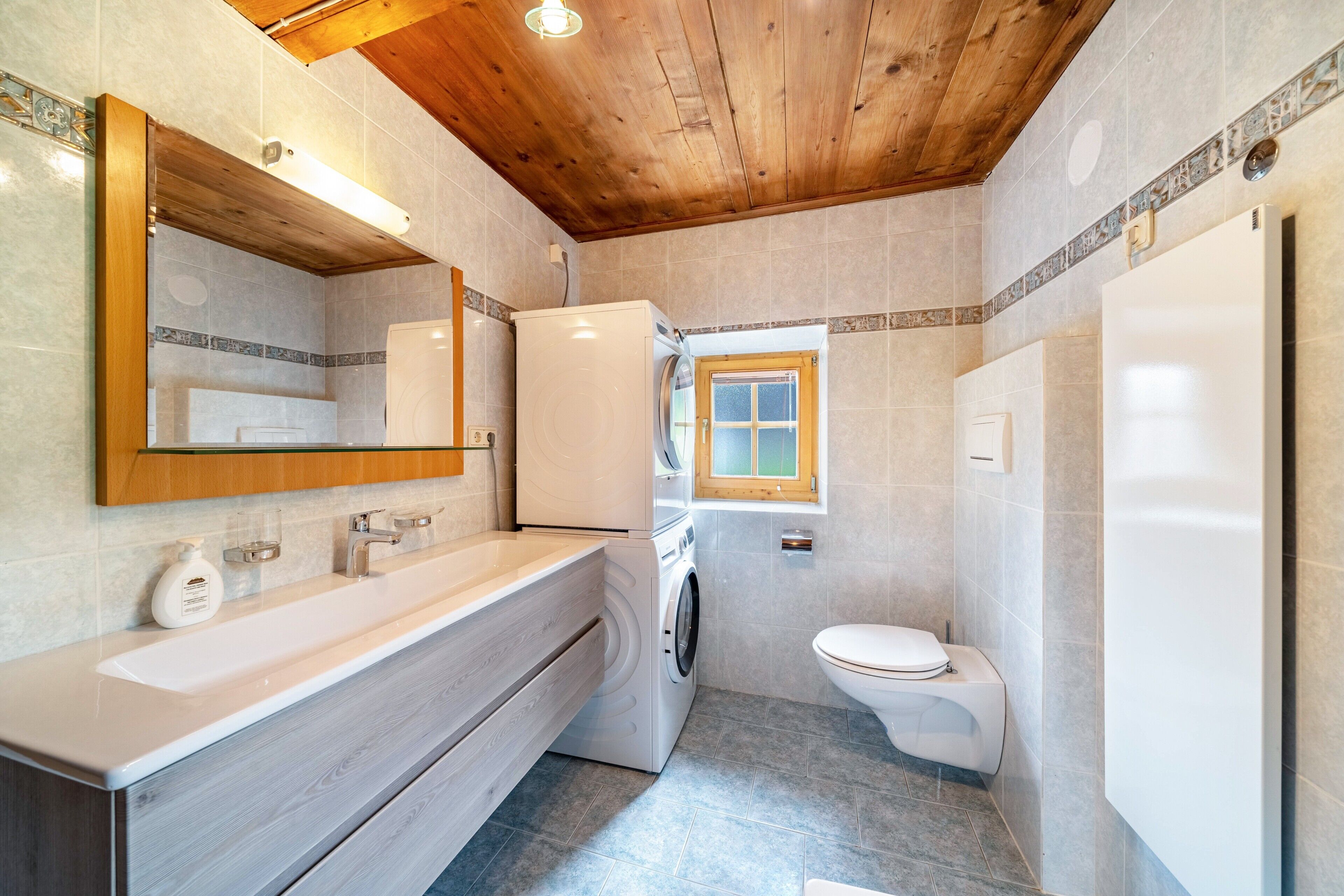 Une salle de bain avec un plafond en bois, un lave-linge, des toilettes et un grand miroir.