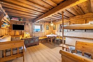 L’intérieur d’une cabane en bois est aménagé avec un lit superposé, un téléviseur, une table avec des chaises et une bibliothèque.