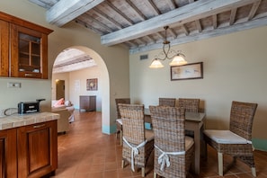 A kitchen with wooden cabinets, a dining area with wicker chairs, and a ceiling with exposed beams. - Hotel Apartment "Olivo" with Shared Pool & Wi-Fi (Trequanda)