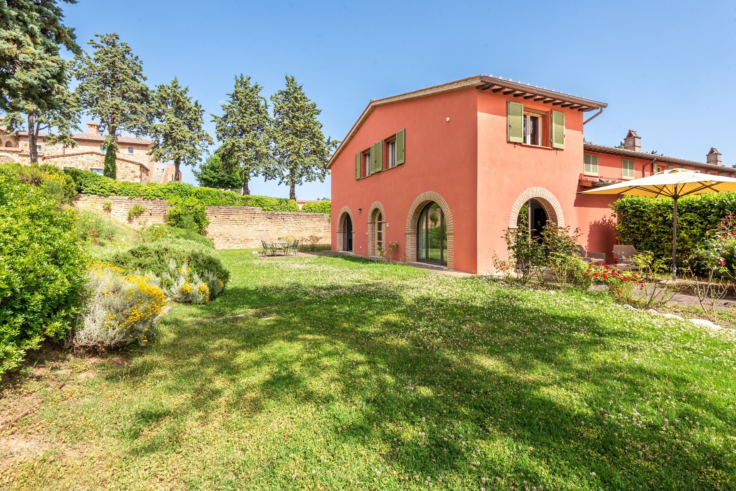 A red building with arched windows and a garden with grass and bushes.