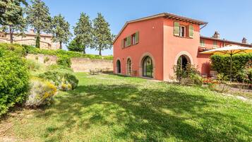 A red building with arched windows and a garden with grass and bushes.
