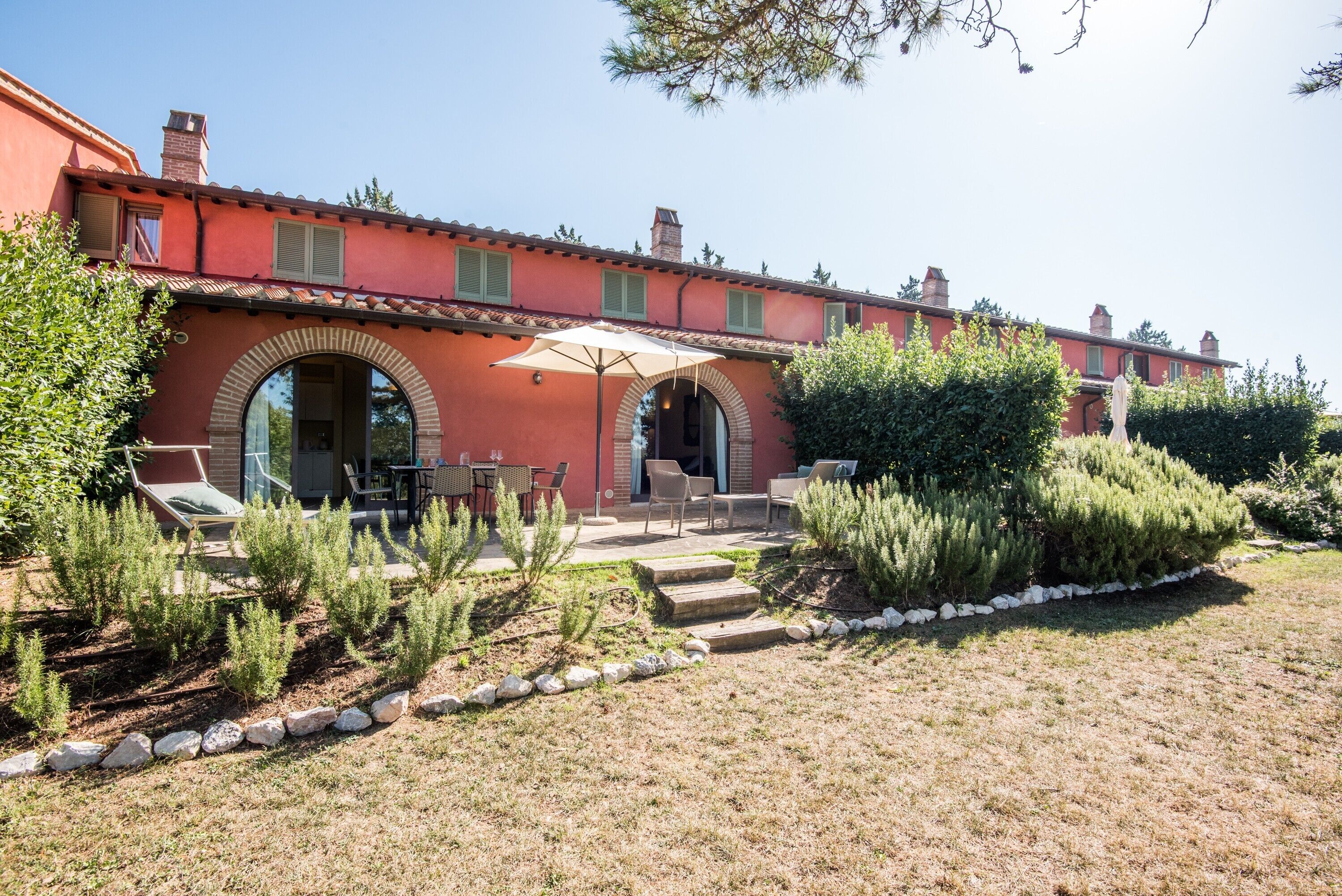 A red villa with outdoor seating, a stone pathway, and a well-maintained garden.