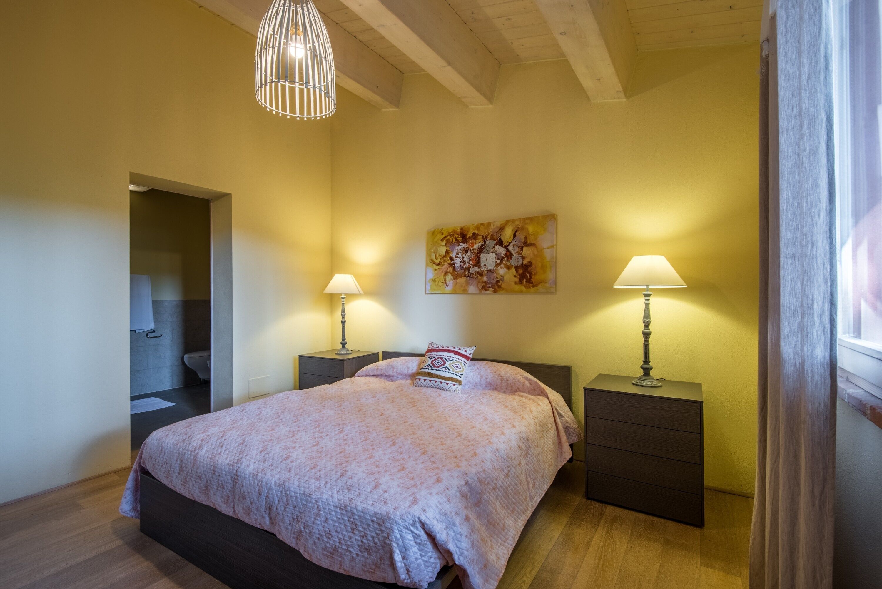 Une chambre à coucher avec un lit, deux tables de chevet avec des lampes, un tableau au mur et un plafond en bois.