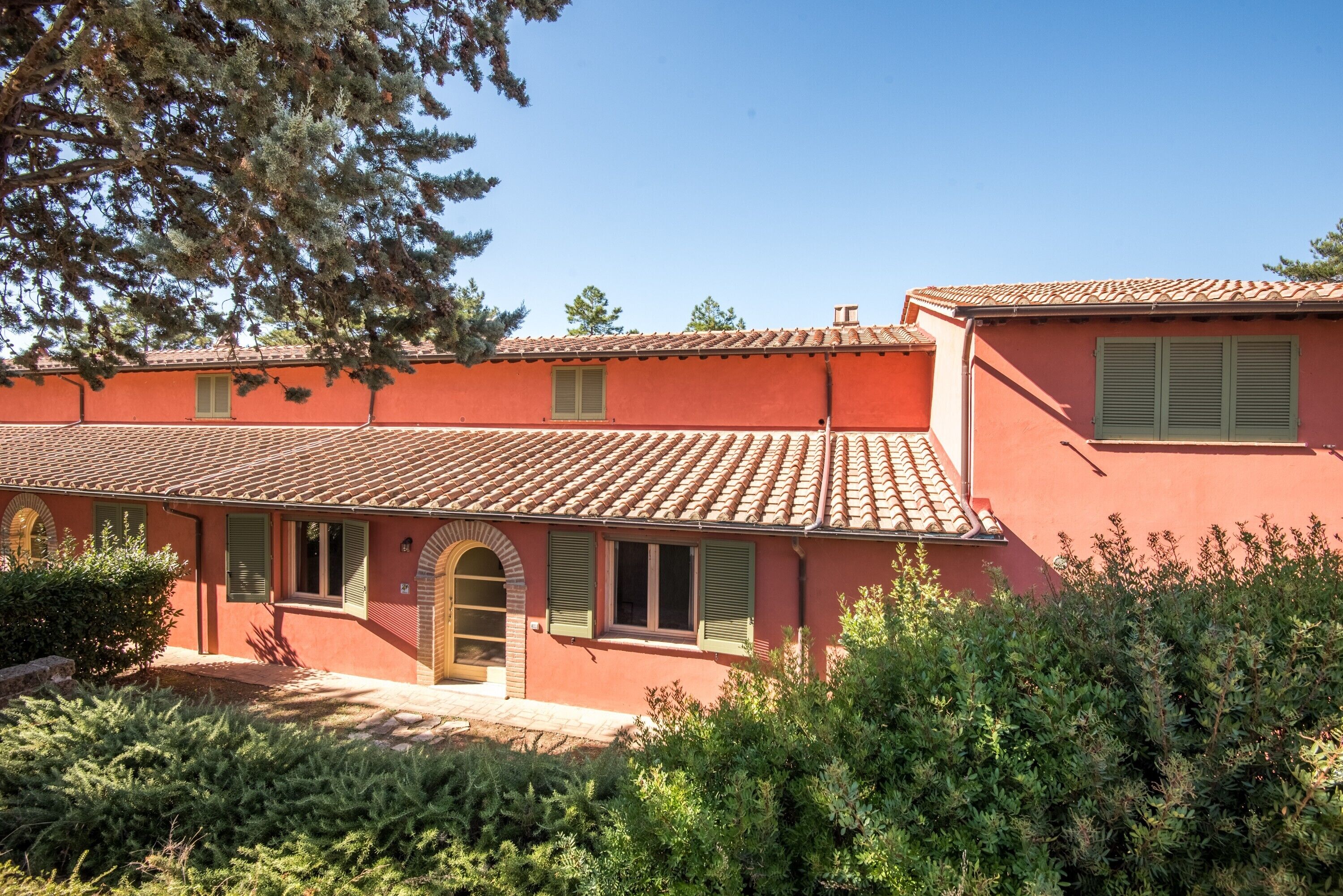 A red building with a tiled roof, arched entrance, and green shutters.