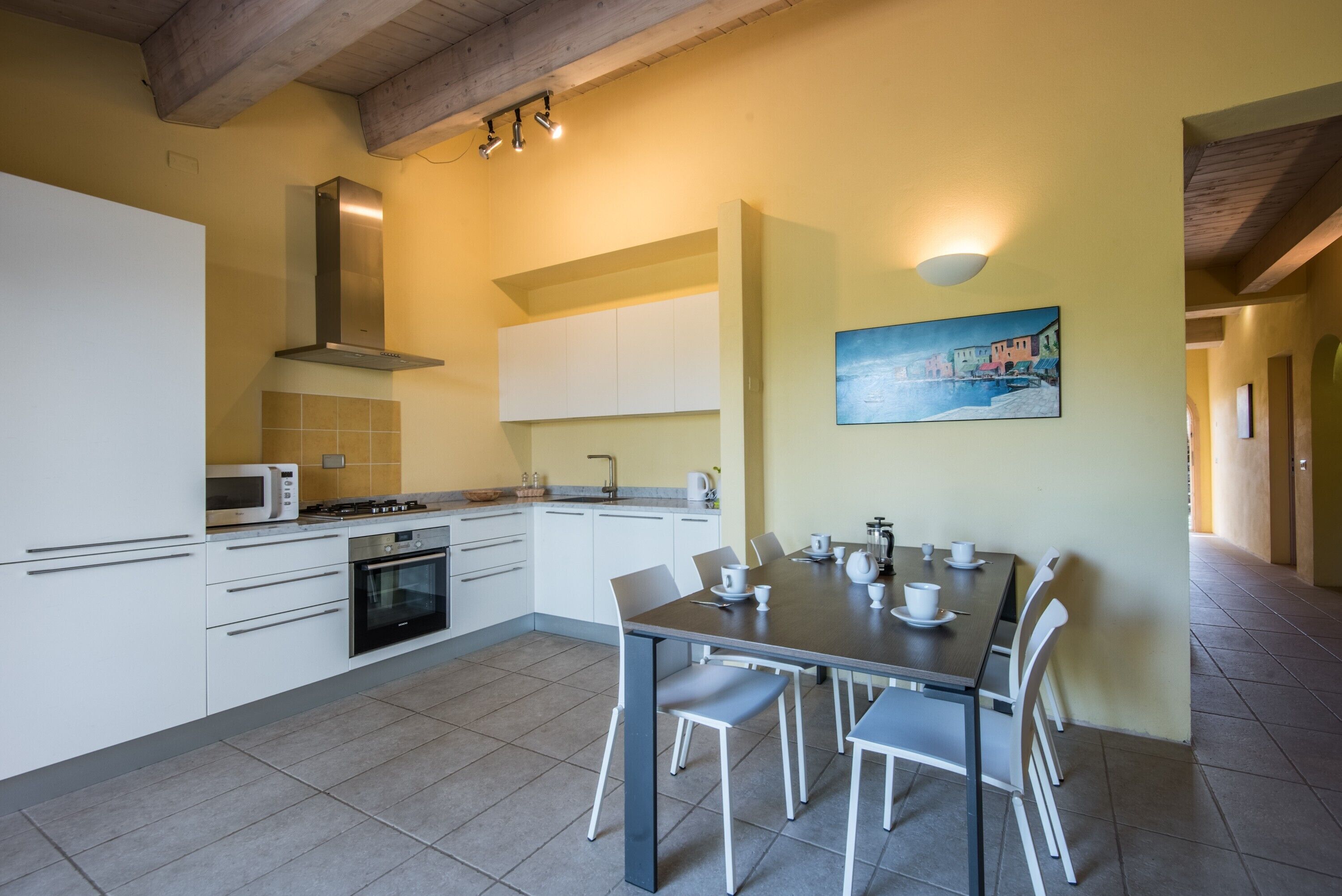 Een moderne keuken met witte kastjes, een eettafel met stoelen en een schilderij aan de muur.