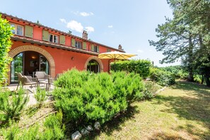 A red building with arched windows, outdoor seating, and a yellow umbrella.