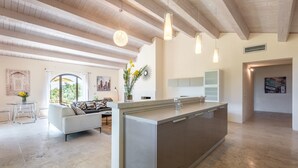 A spacious living area with a large island kitchen, wooden ceiling beams, and a dining area with a table and chairs.
