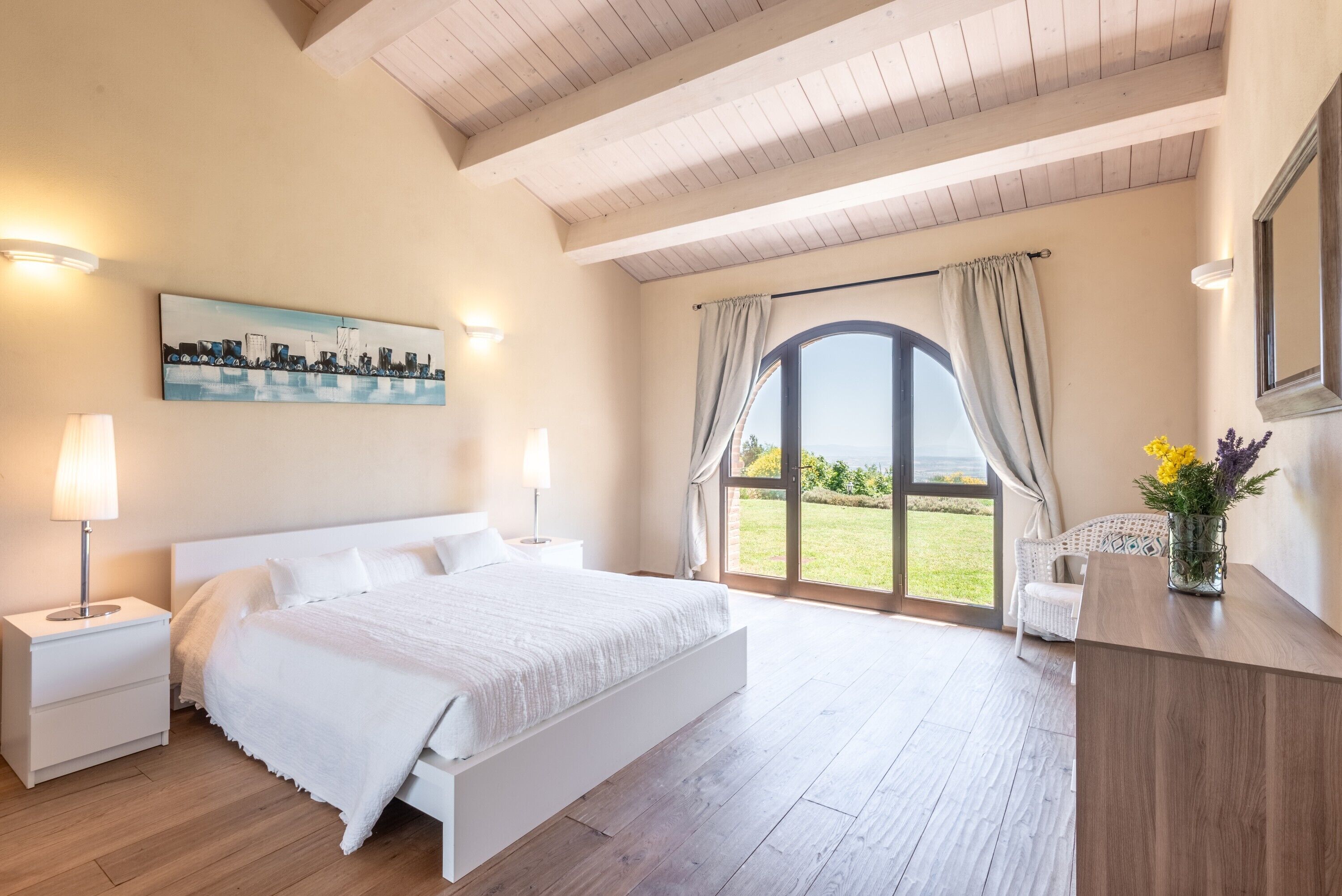 A bedroom with a bed, nightstands, a painting, a window with curtains, and a view of the outdoors.