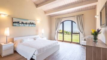 A bedroom with a bed, nightstands, a painting, a window with curtains, and a view of the outdoors.