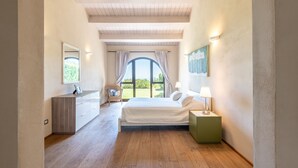 A bedroom with a bed, bedside table, lamp, and a view of the outdoors.