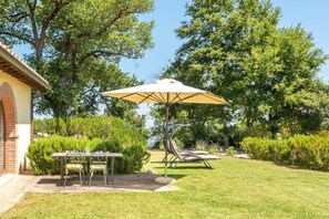 Un patio con una mesa, sillas y una sombrilla grande, además de una silla con cojines.