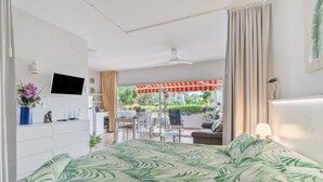 Un dormitorio con cama, televisión, escritorio y balcón con mobiliario exterior.