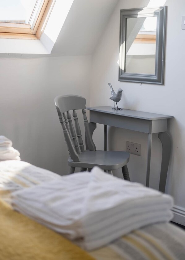 Un dormitorio con cama, una silla, un escritorio y un tragaluz.