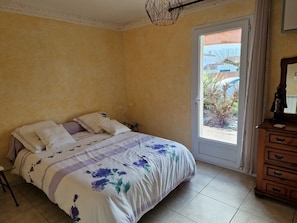 A bedroom with a bed, a dresser, a door leading to an outdoor area, and a ceiling light fixture.