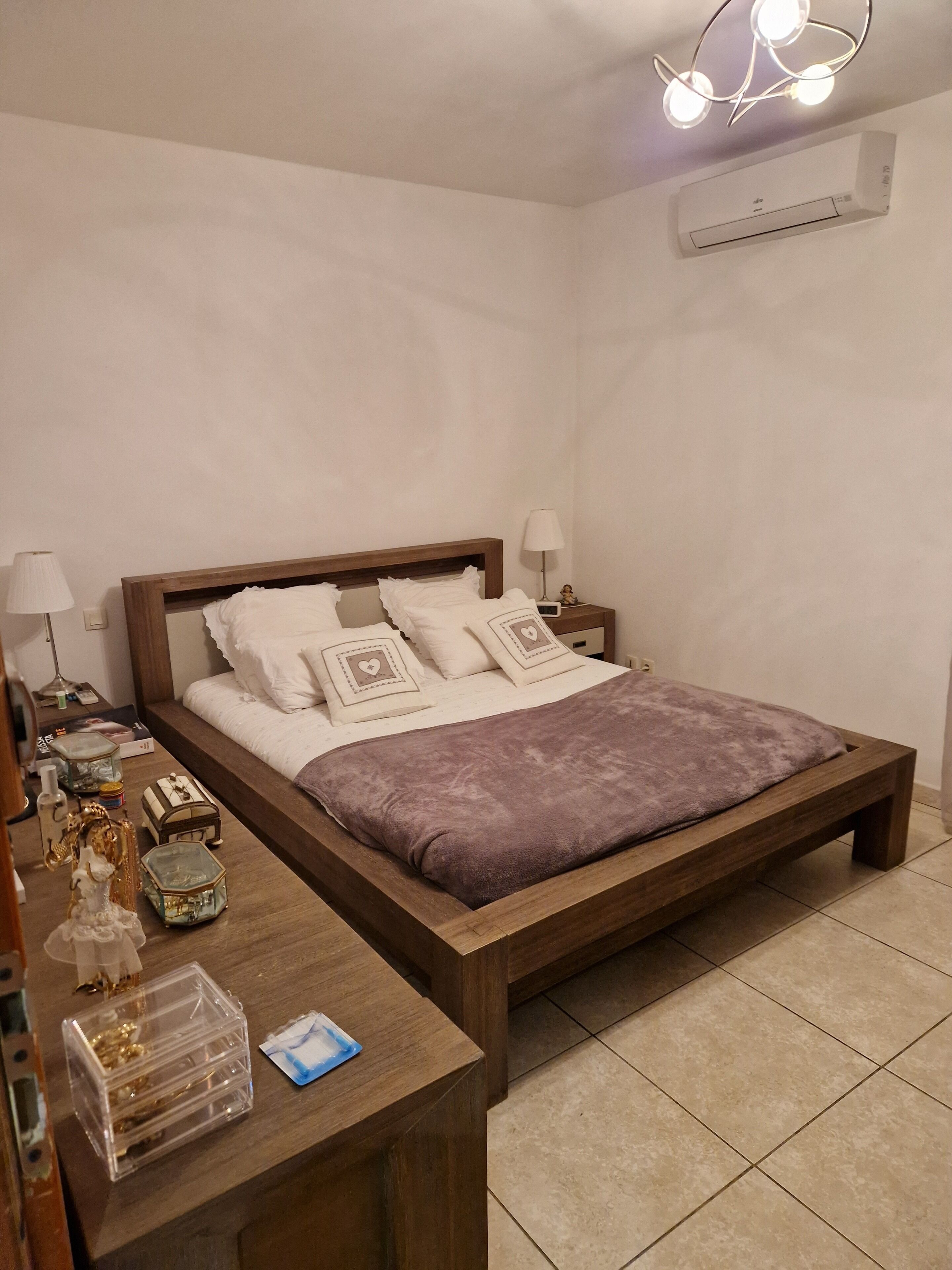 A neatly arranged bedroom with a wooden bed, bedside lamps, a nightstand, and a small table with decorative items.