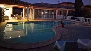 Ein Pool mit gewölbter Kante, eine überdachte Terrasse mit Sitzgelegenheiten und ein weißer Zaun rund um den Pool.