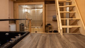 Un intérieur en bois comprenant un espace cuisine, un escalier en bois et un sauna visible à travers une porte en verre.