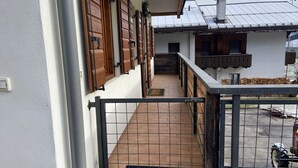 Een balkon met een metalen hekwerk, houten luiken en uitzicht op een gebouw met een pannendak.