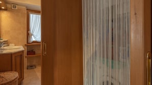 Een houten deur met een witte gordijn, die leidt naar een badkamer met een wastafel, een weegschaal en een rieten mand.