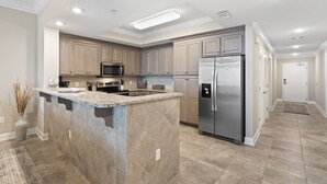 Une cuisine moderne dotée de plans de travail en granit, d’appareils électroménagers en acier inoxydable et de meubles de couleur beige.