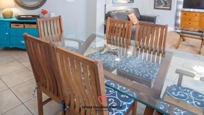 A dining area with a glass table, wooden chairs, and a chandelier. - Pier Walk B ~ 2 Kings, 1 Queen, 2 Twins, 3 cars (Tybee Island)