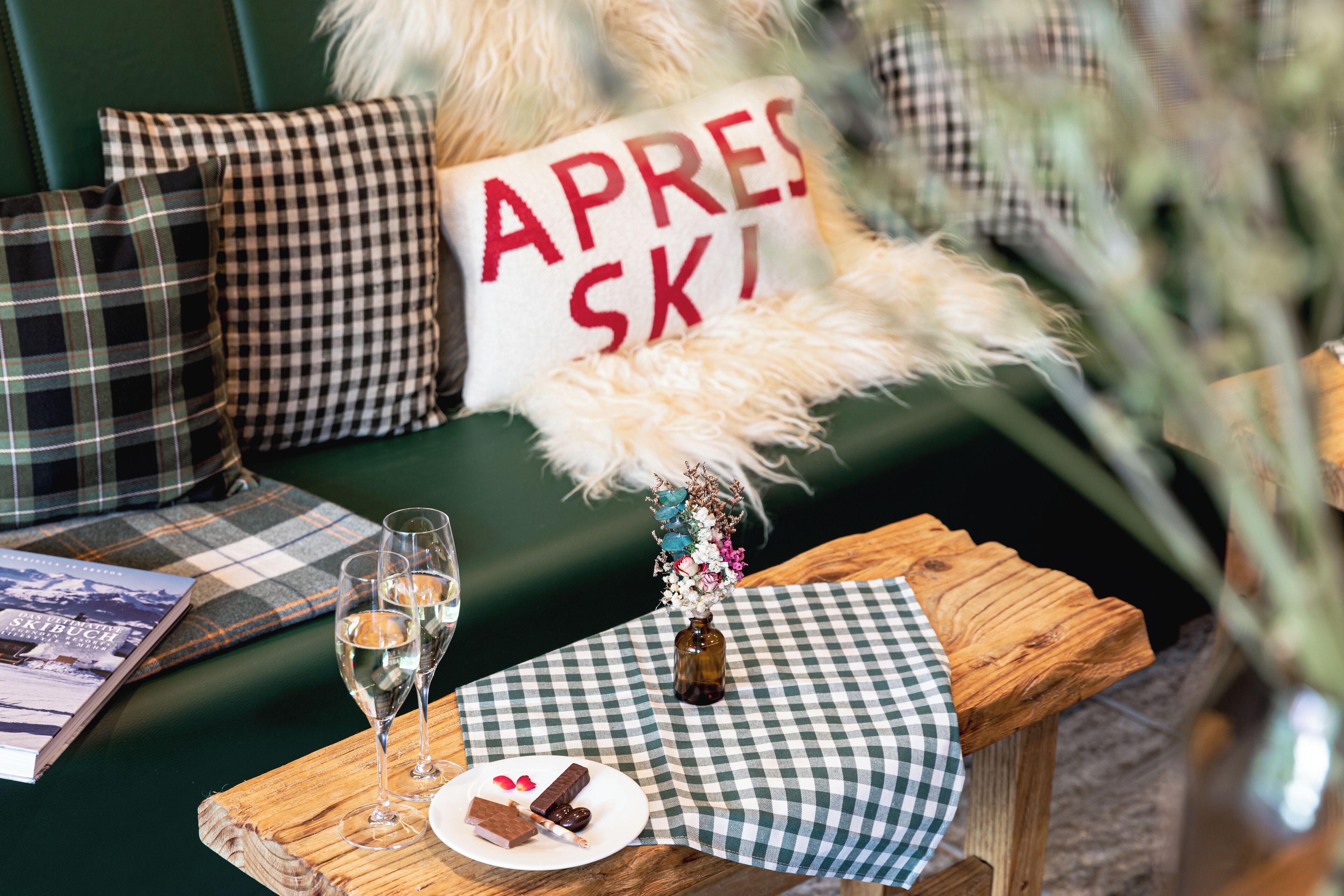 A cozy seating area with a checkered tablecloth, a bottle of wine, glasses, and a plate with a dessert.