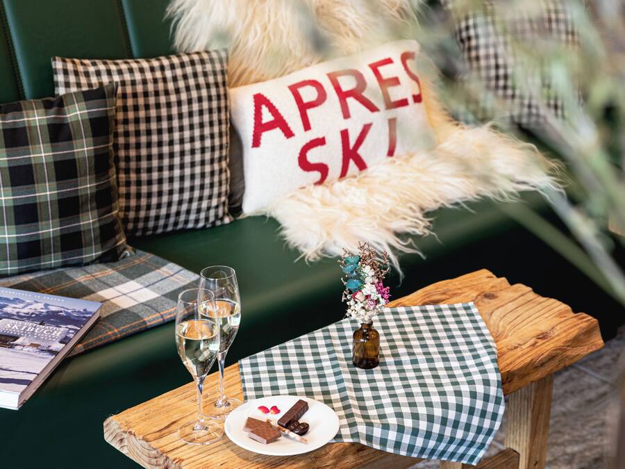 A cozy seating area with a checkered tablecloth, a bottle of wine, glasses, and a plate with a dessert.