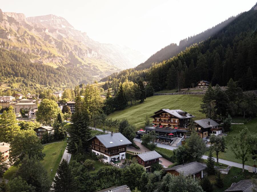 A mountain resort with chalet-style buildings, a ski lift, and a lush green valley.