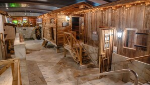 A rustic cabin-style room with wooden walls, a stone floor, and a wooden staircase. - Hotel Waldhaus (Leukerbad)