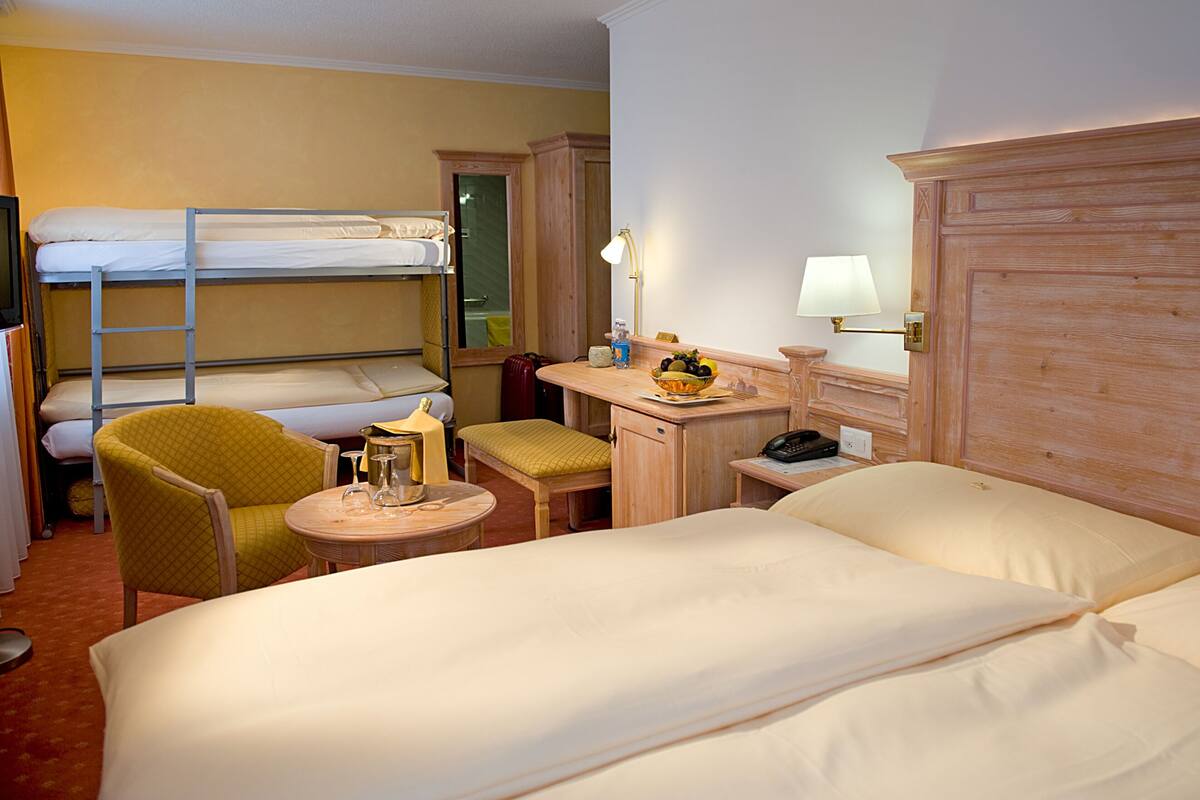 Habitación de hotel con literas, un escritorio con lámpara, una silla y una pequeña mesa con un bol de fruta.