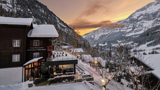 A hotel building with a sign reading "Hotel Restaurant WALDHAUS GRICHTING" and a glass-roofed structure with outdoor seating. - Hotel Waldhaus (Leukerbad)