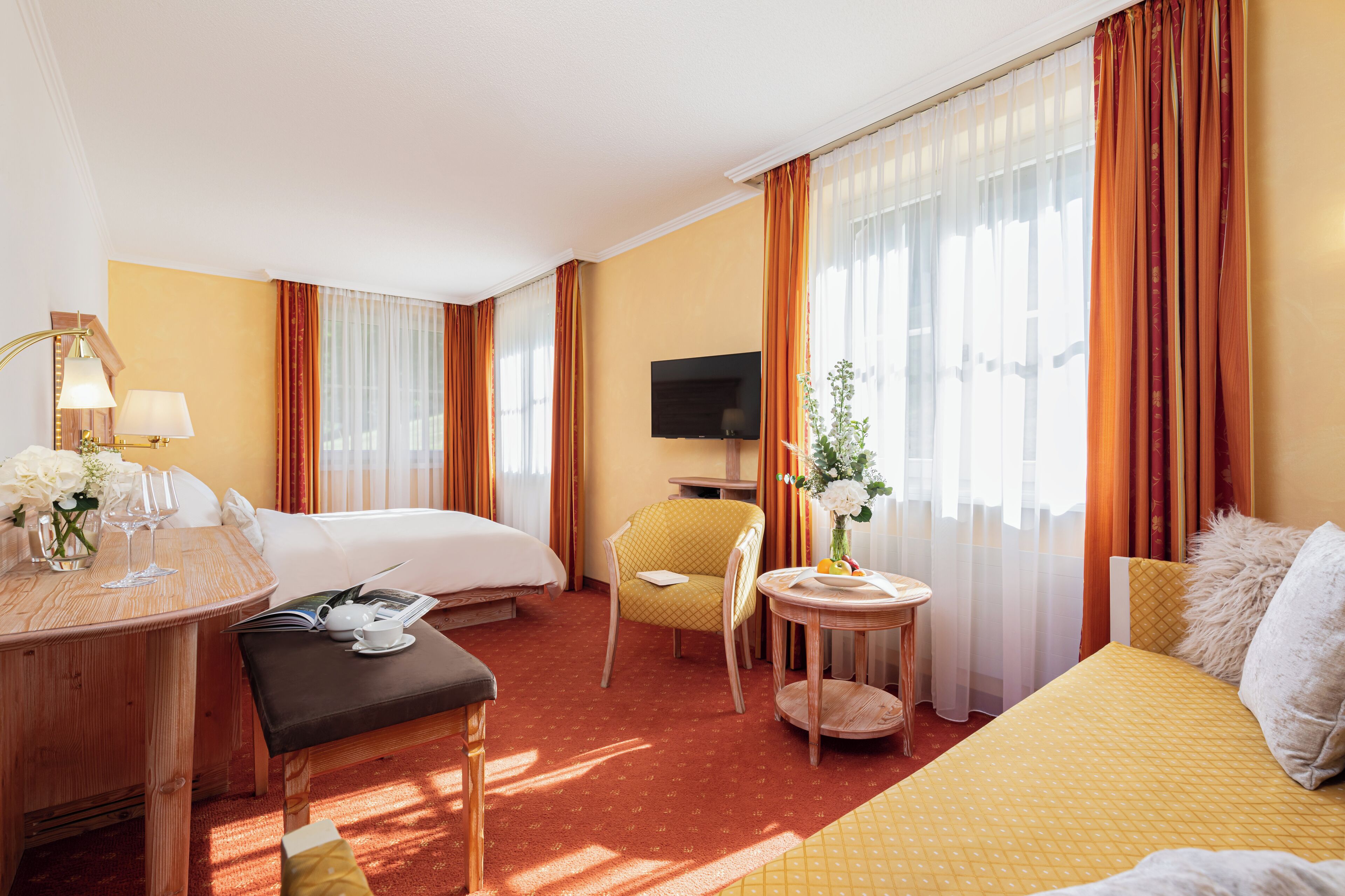Une chambre d’hôtel comprenant un lit, un bureau avec une lampe, une chaise, une petite table avec un vase et un téléviseur.