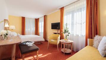 Une chambre d’hôtel comprenant un lit, un bureau avec une lampe, une chaise, une petite table avec un vase et un téléviseur.