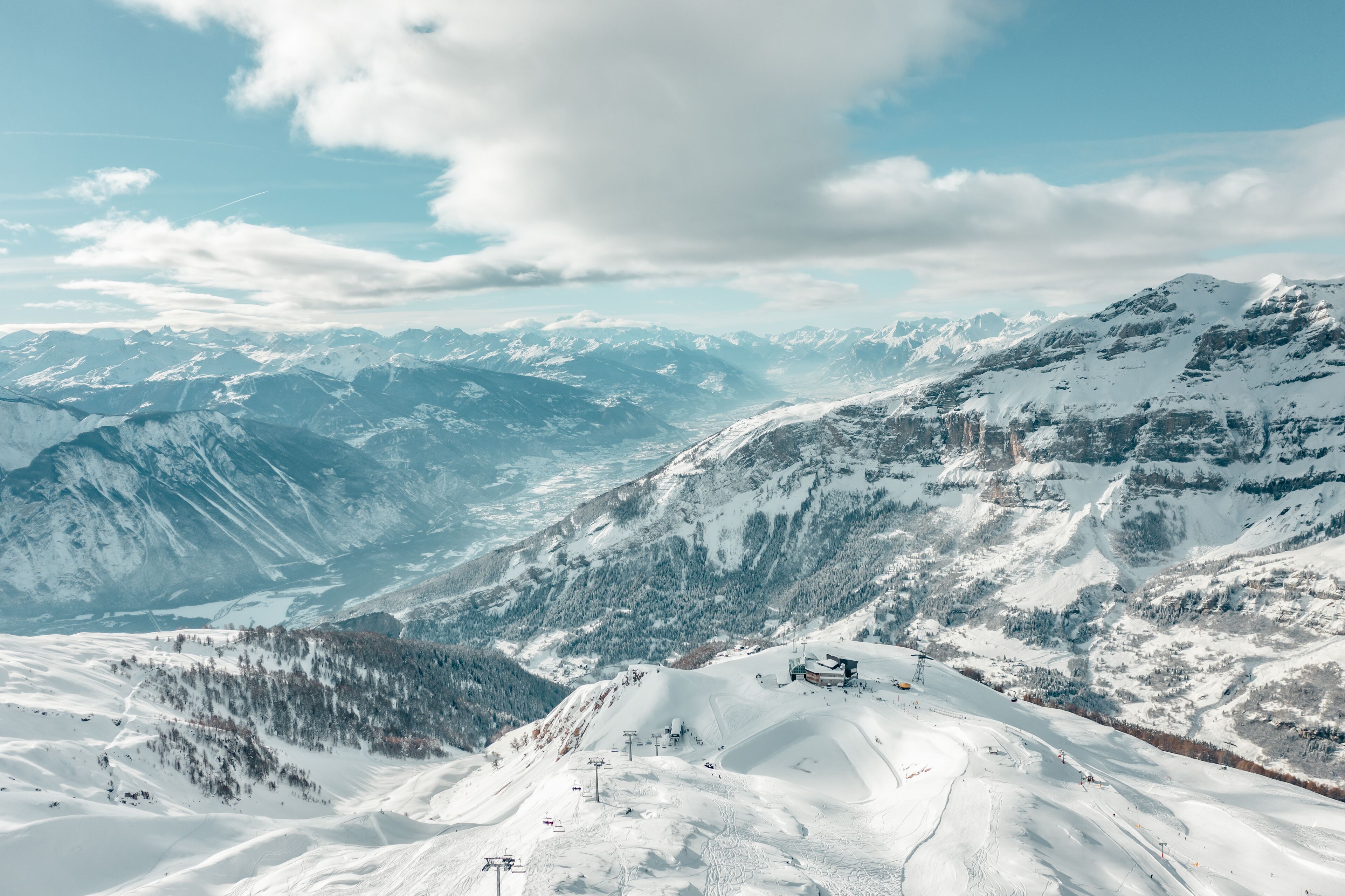 Paesaggio montano innevato con una stazione sciistica, incluse seggiovie e un rifugio.