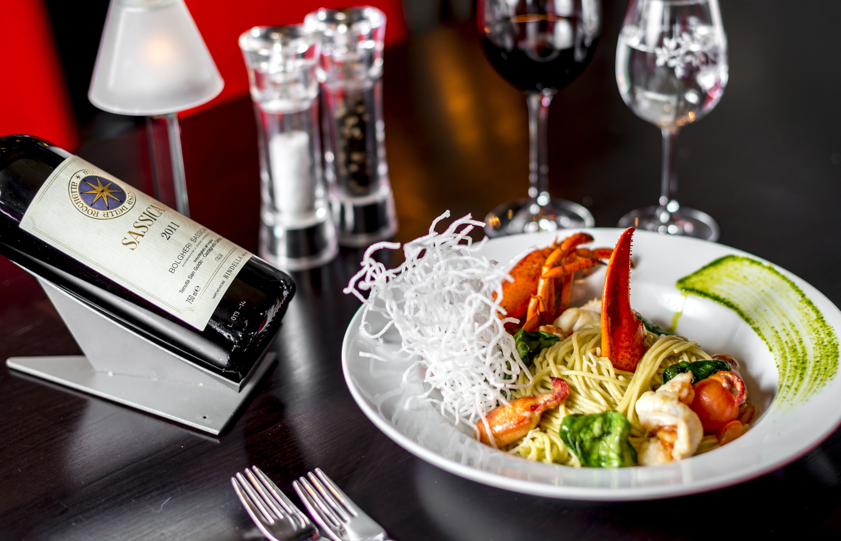 A dining table with a plate of food, a bottle of wine, and salt and pepper shakers.