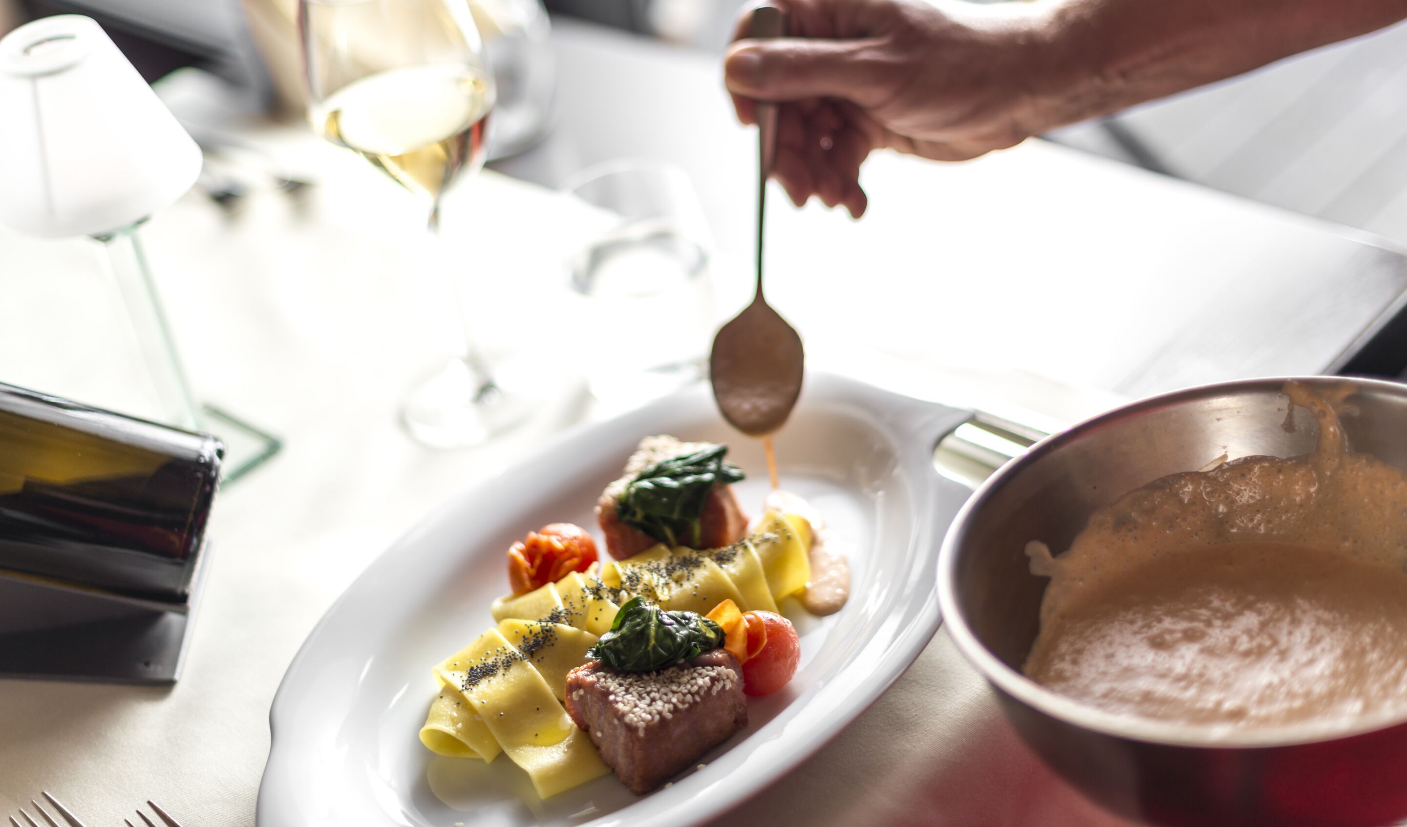 Una persona sirve comida en un plato blanco con pasta, un trozo de carne y verduras.