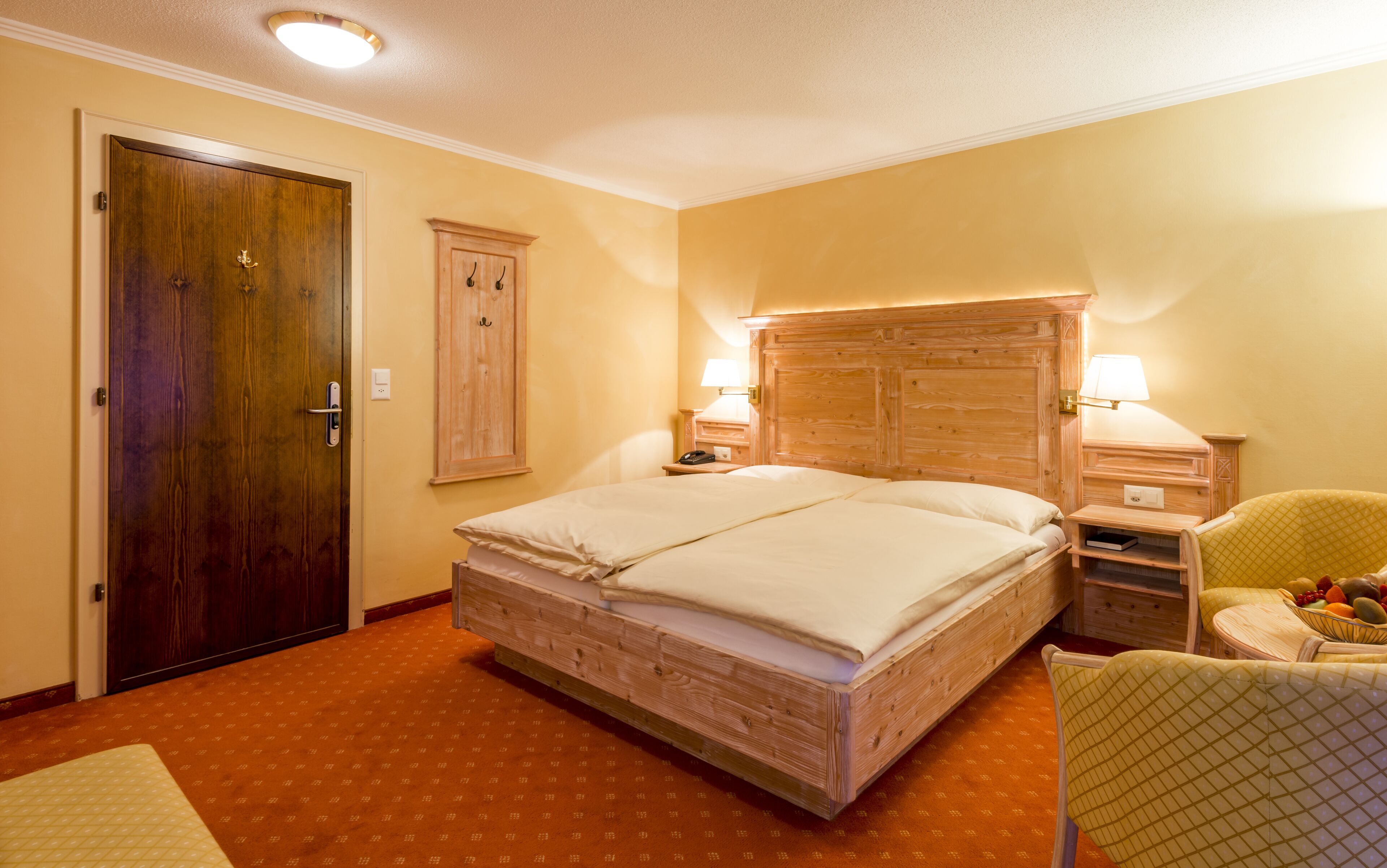 A hotel room with a wooden bed, two bedside tables with lamps, a chair, and a wardrobe.