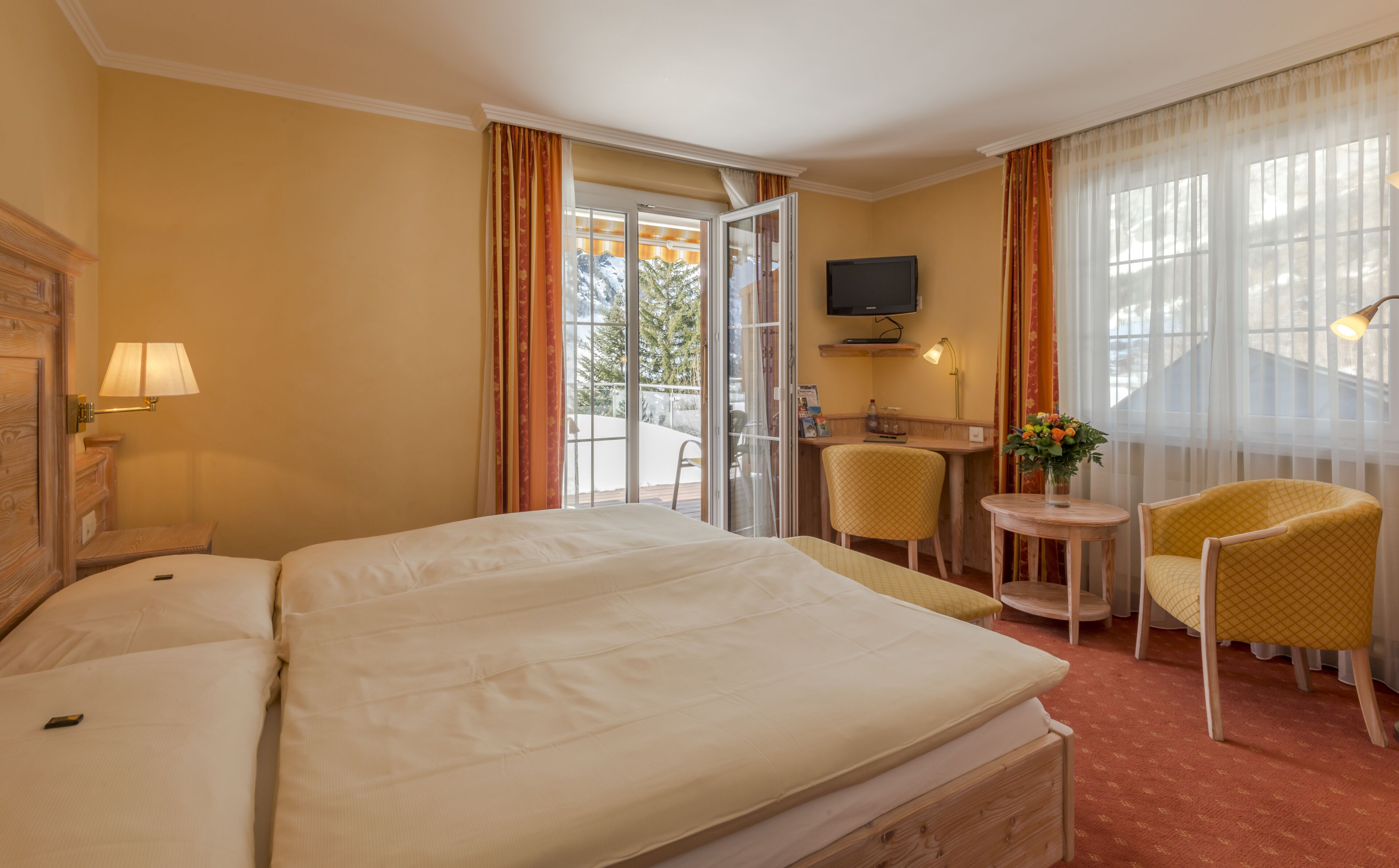 A hotel room with a large bed, a desk with a chair, a television, and a view of the outdoors.